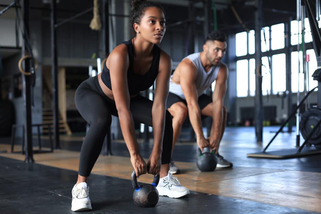 Entraînement Kettlebell : Force et Fitness en Salle Femme et homme musclés soulevant des kettlebells de 12 kg dans une salle de sport. Ils sont concentrés sur leur entraînement de force.